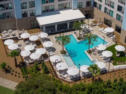Aerial view of hotel pool decks with white umbrellas, lounge chairs, and surrounding landscaping