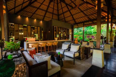 Open-air tropical resort pavilion with wooden ceiling, bar, lounge seating and lush greenery