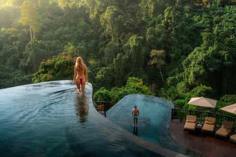 Infinity pool overlooking dense forest canopy with guests swimming at luxury jungle resort
