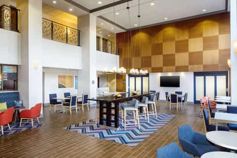 Multi-story hotel atrium lobby with gold wood accents, dining tables, lounge seating, and modern architecture