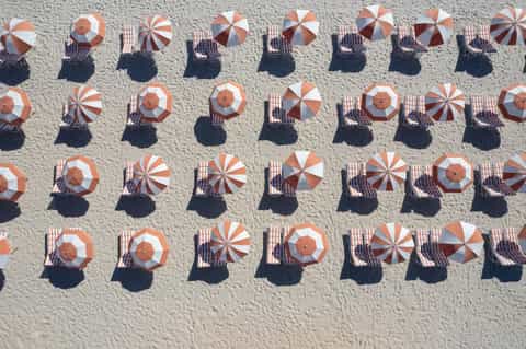 Aerial view of beach with rows of red and white striped umbrellas and sunbathers