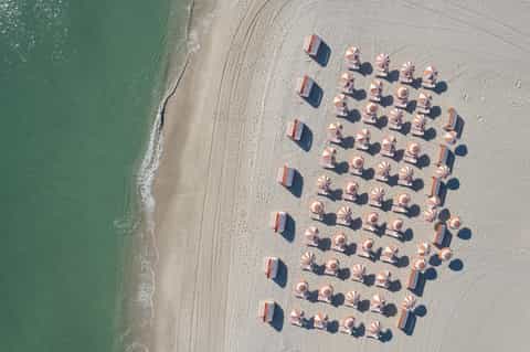 Aerial view of organized beach with red and white striped umbrellas and lounge chairs on sand
