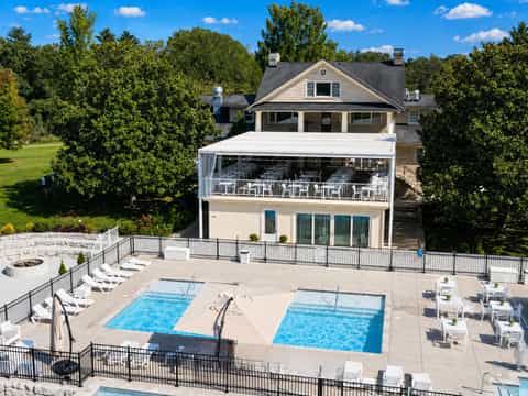 Aerial view of luxury home with multiple pools, deck, and surrounding greenery