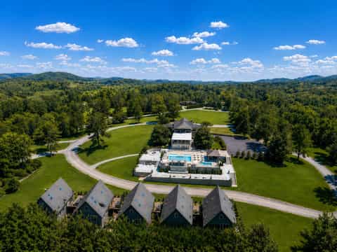 Aerial view of resort property with pools, guest cottages, and forested landscape