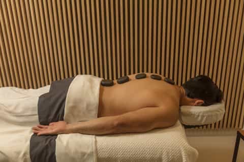 Man receiving hot stone massage therapy on his back in spa treatment room