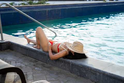 Woman in red bikini lounging by resort swimming pool wearing straw hat
