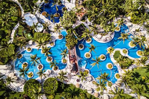 Aerial view of tropical resort pool complex with palm trees and lounging areas