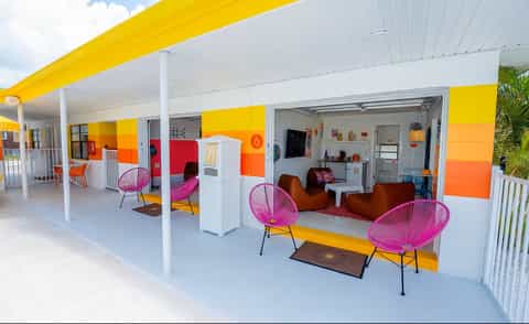 Vibrant outdoor lounge area with yellow and orange striped awning, pink wire chairs, brown bean bags, and white columns