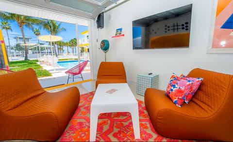 Bright indoor lounge space with orange seating, pool view through open doors, and vibrant tropical decor