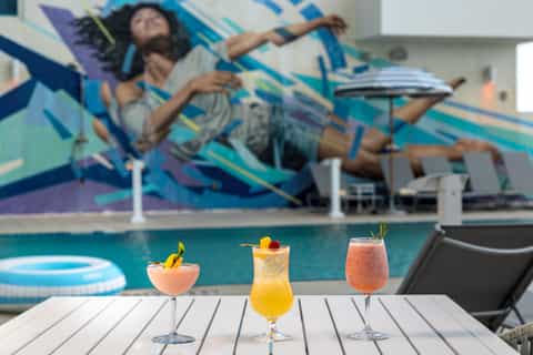 Tropical cocktails on poolside table with mural backdrop and lounging guest