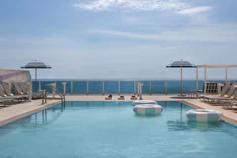 Resort rooftop pool with striped umbrellas, loungers, and ocean horizon views