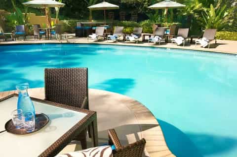 Resort pool with crystal-clear blue water, lounge chairs, umbrellas, and tropical landscaping