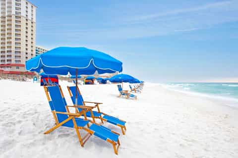 Sandy beach with blue umbrellas and wooden loungers facing ocean and beachfront hotels