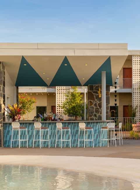 Modern poolside bar with teal geometric awning, white seating, and contemporary architecture