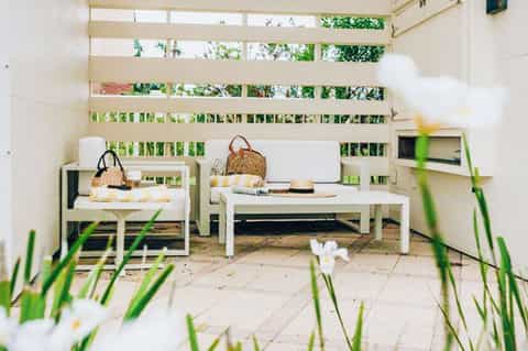 Minimalist white patio seating area with lounge chairs and slatted privacy screens surrounded by greenery
