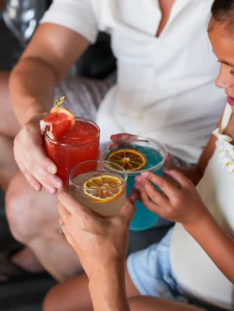 Close-up of tropical cocktails with fresh fruit garnish held by people in white clothing