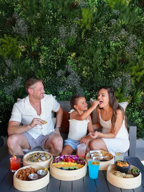 Family dining outdoors against lush green living wall with fresh fruit platters and colorful beverages