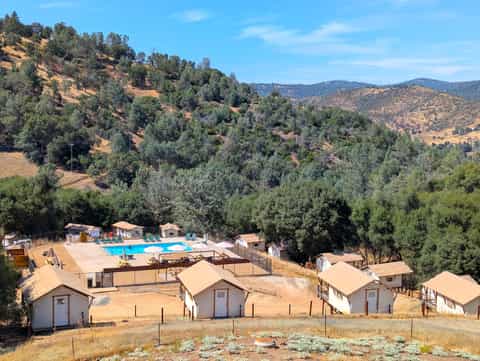 Aerial view of glamping resort with pool, cabins, and forested hillside landscape