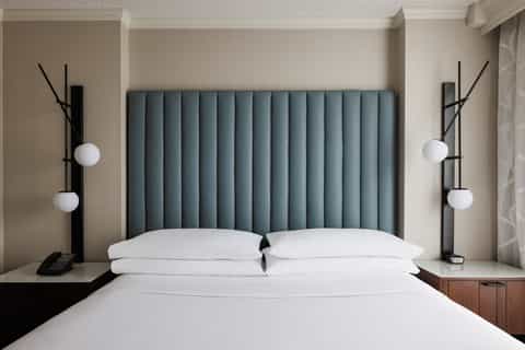 Modern hotel bedroom with teal upholstered headboard, white pillows, and contemporary black bedside lamps