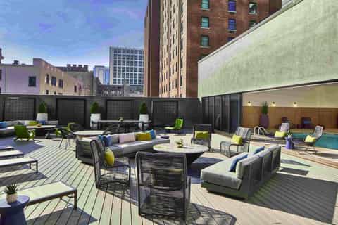 Rooftop terrace with lounge seating, fire pit, pool, and city skyline views surrounded by modern buildings