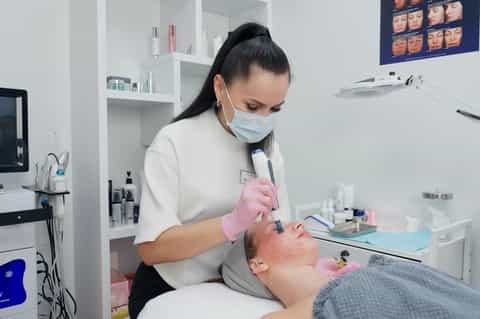 Aesthetician applying facial treatment with handheld device in modern spa clinic