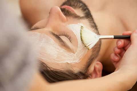 Esthetician applying white face mask to male client with cosmetic brush