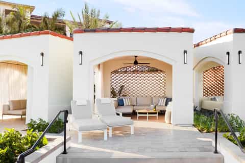 Mediterranean-style resort courtyard with white arches, lounge seating, and palm trees
