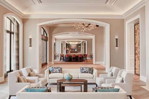 Elegant living room with beige furnishings, arched doorways, and view into bar area with high ceilings