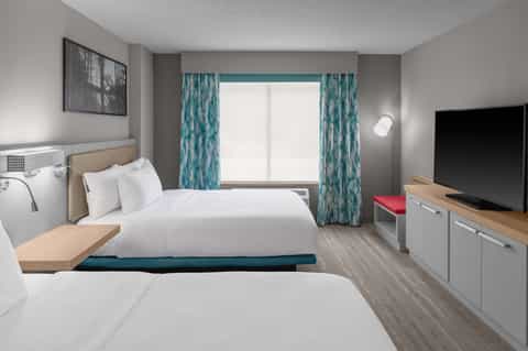 Hotel guest room with two queen beds, teal patterned curtains, TV, and modern furnishings