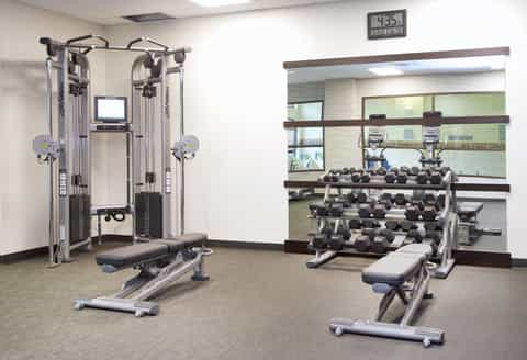 Fitness center with cardio equipment, weight machines, dumbbells, mirrors, and digital clock on wall