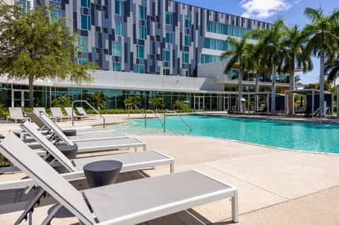 Modern resort pool with turquoise water, lounge chairs, and contemporary high-rise building with palm trees