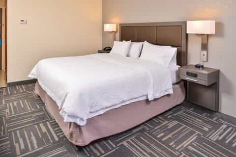 Single queen bed with white bedding in a hotel room with brown headboard and geometric patterned carpet