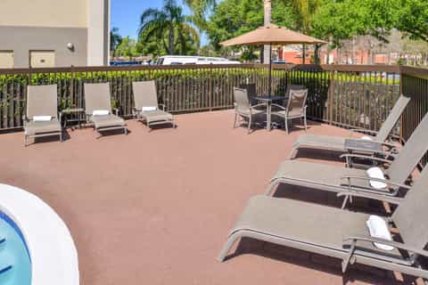 Poolside deck with lounge chairs, umbrellas, seating area, and resort grounds with palm trees