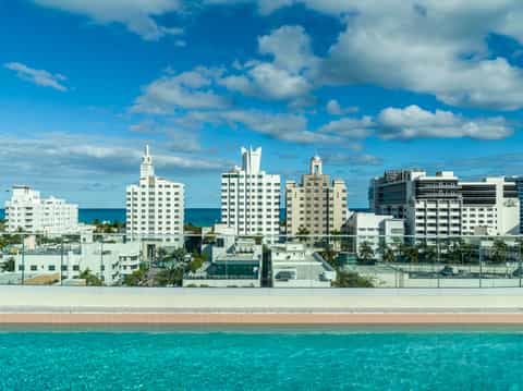 Beachfront Miami hotel skyline with Art Deco buildings, turquoise ocean, and white sandy beach under blue sky