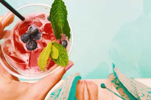 Pink berry cocktail with fresh blueberries and mint leaves in tropical setting