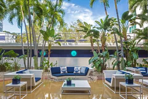 Tropical courtyard with palm trees, blue water feature, white lounge seating with navy cushions, and modern building backdrop