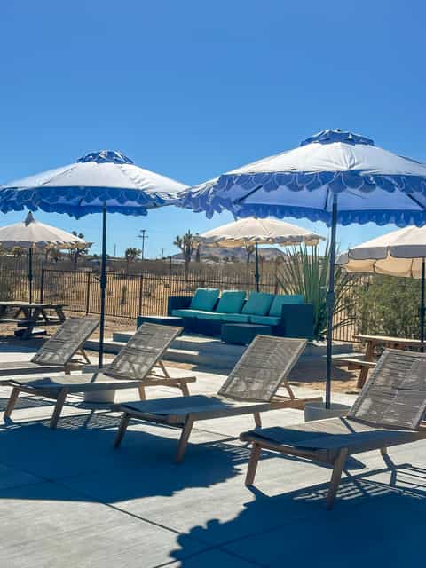 Lounge area with striped chairs, blue and white umbrellas, and teal seating under desert sky