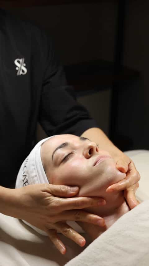 Facial massage treatment with hands on client's face wearing white headband