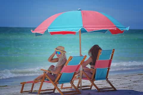 Two women in beach chairs under a pink and blue umbrella in the ocean