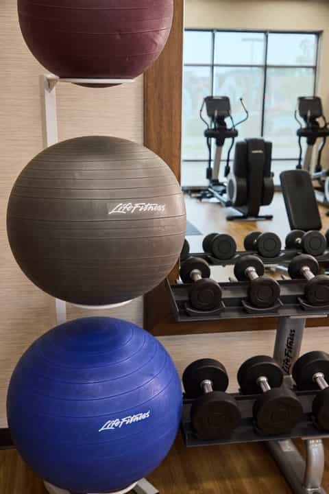 Fitness studio detail showing exercise balls and dumbbells with gym equipment and windows in background