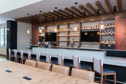 Hotel bar lounge with wooden beam ceiling, white marble counter, leather seating, and fully stocked liquor shelves with TVs