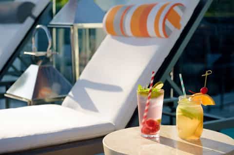 Two colorful tropical cocktails on a poolside table with lounge chairs in background