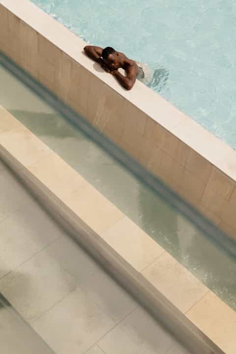 Man relaxing at the edge of a turquoise swimming pool with tiled surroundings and clear water