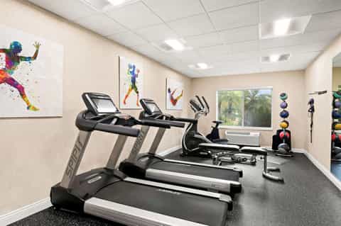 Modern fitness center with treadmills, exercise bikes, colorful motivational wall art, and windows