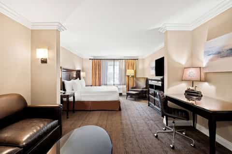 Spacious hotel suite with king bed, seating area, fireplace, dark wood furniture, and work desk