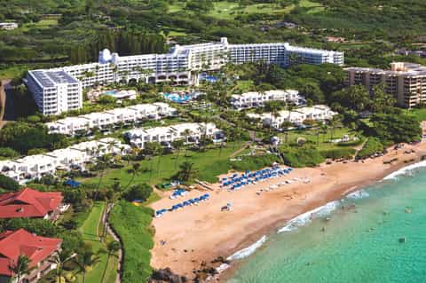 Aerial view of beachfront resort with white buildings, manicured grounds, and turquoise ocean