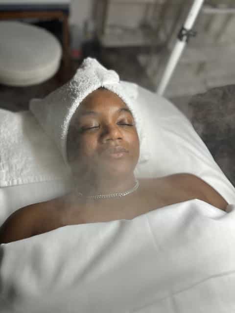 Client with towel wrap and headband lying on spa bed during facial treatment session