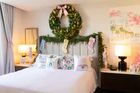 Bedroom with decorated headboard featuring garland and pink bows, matching wreath above, and holiday pillows