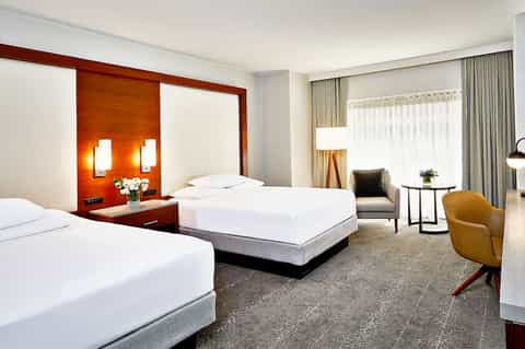 Modern hotel room with two beds, orange accent wall, and contemporary furnishings