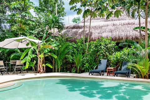 Tropical resort pool surrounded by lush vegetation and thatched-roof structures